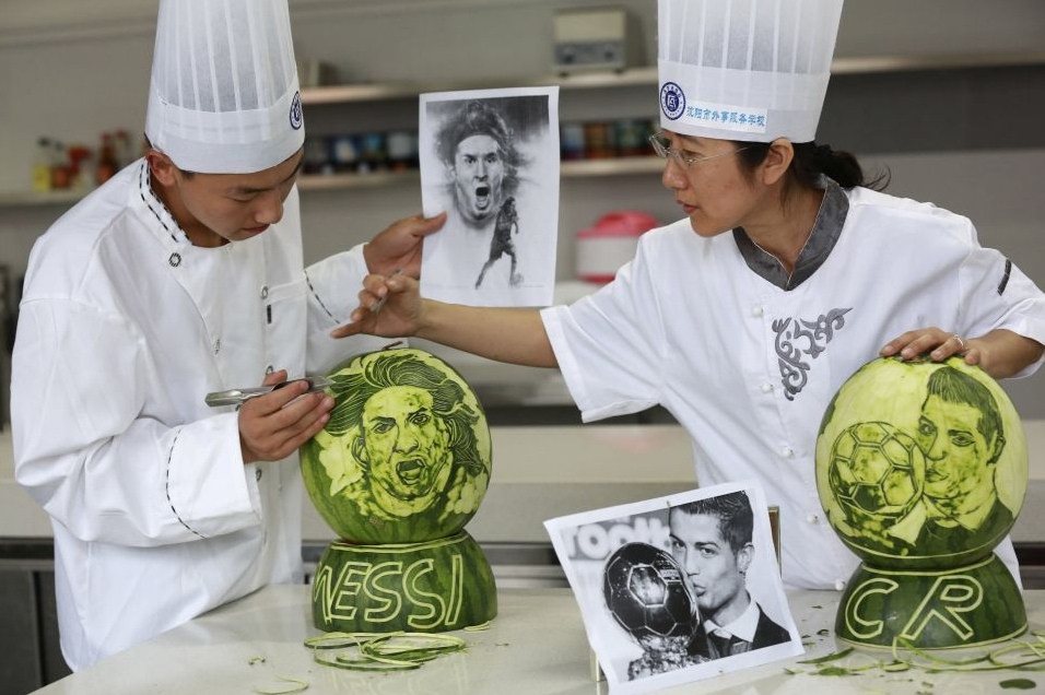 Повар и ее ученик вырезают на арбузах портреты Лионеля Месси и Криштиану Роналду в честь начала Чемпионата мира по футболу в Бразилии, Шэньян, провинция Ляонин. 