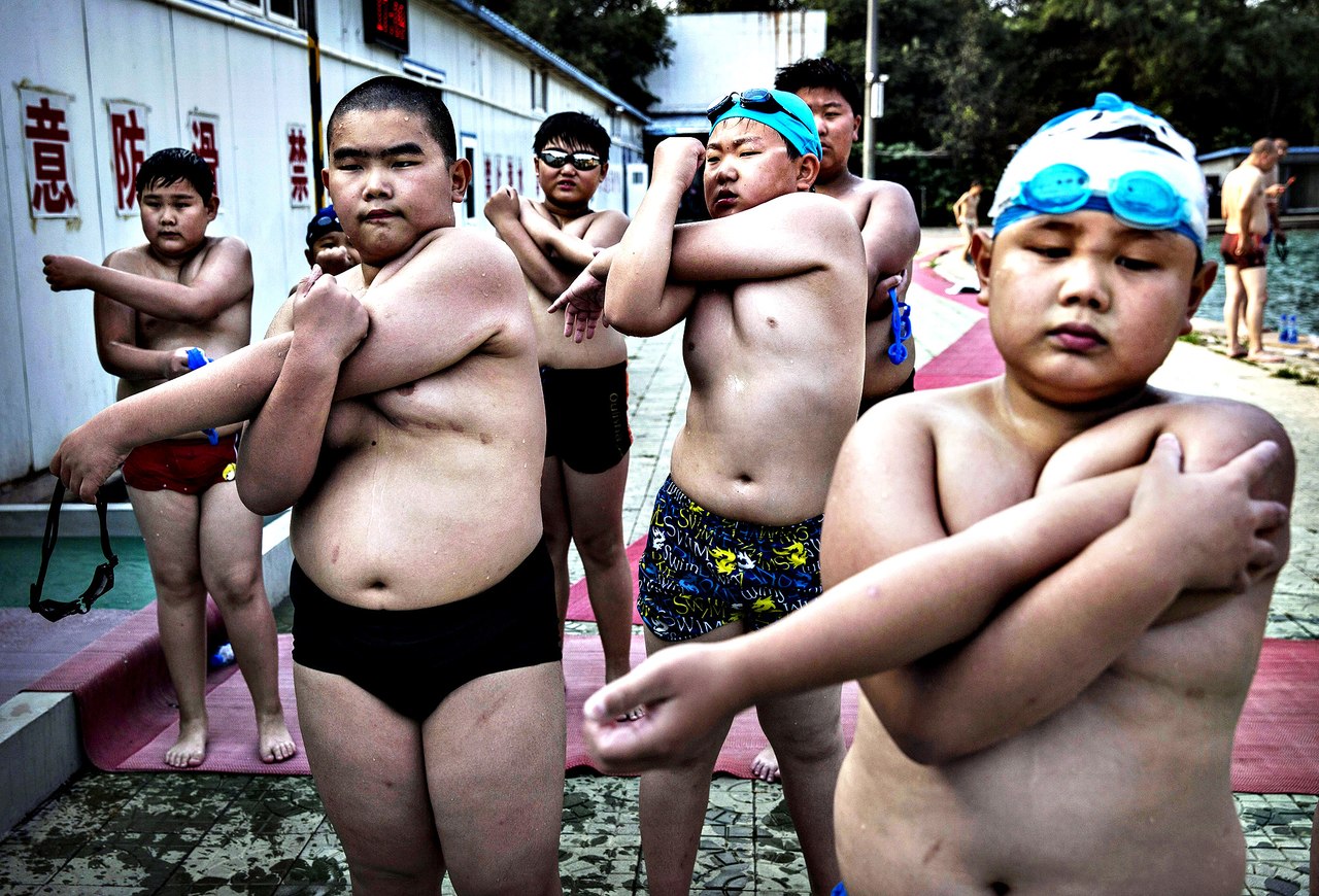 Китайские школьники делают растяжку после плавания в оздоровительном лагере для детей, страдающих лишним весом. Пекин.