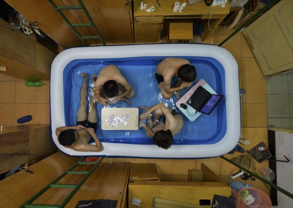 Студенты спасаются от жары в надувном бассейне, поставленном в комнате общежития, Ухань, провинция Хубэй.
