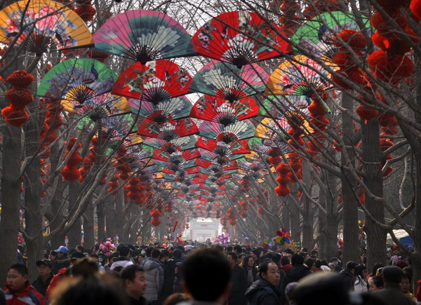Толпы людей под деревьями, украшенных веерами и красными фонарями, в пекинском храме в честь Китайского нового года