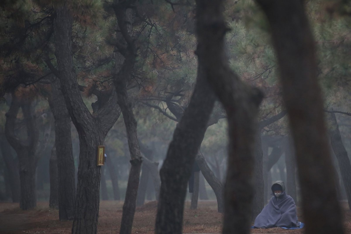Буддист в маске от смога медитирует в парке Храма Неба, Пекин.