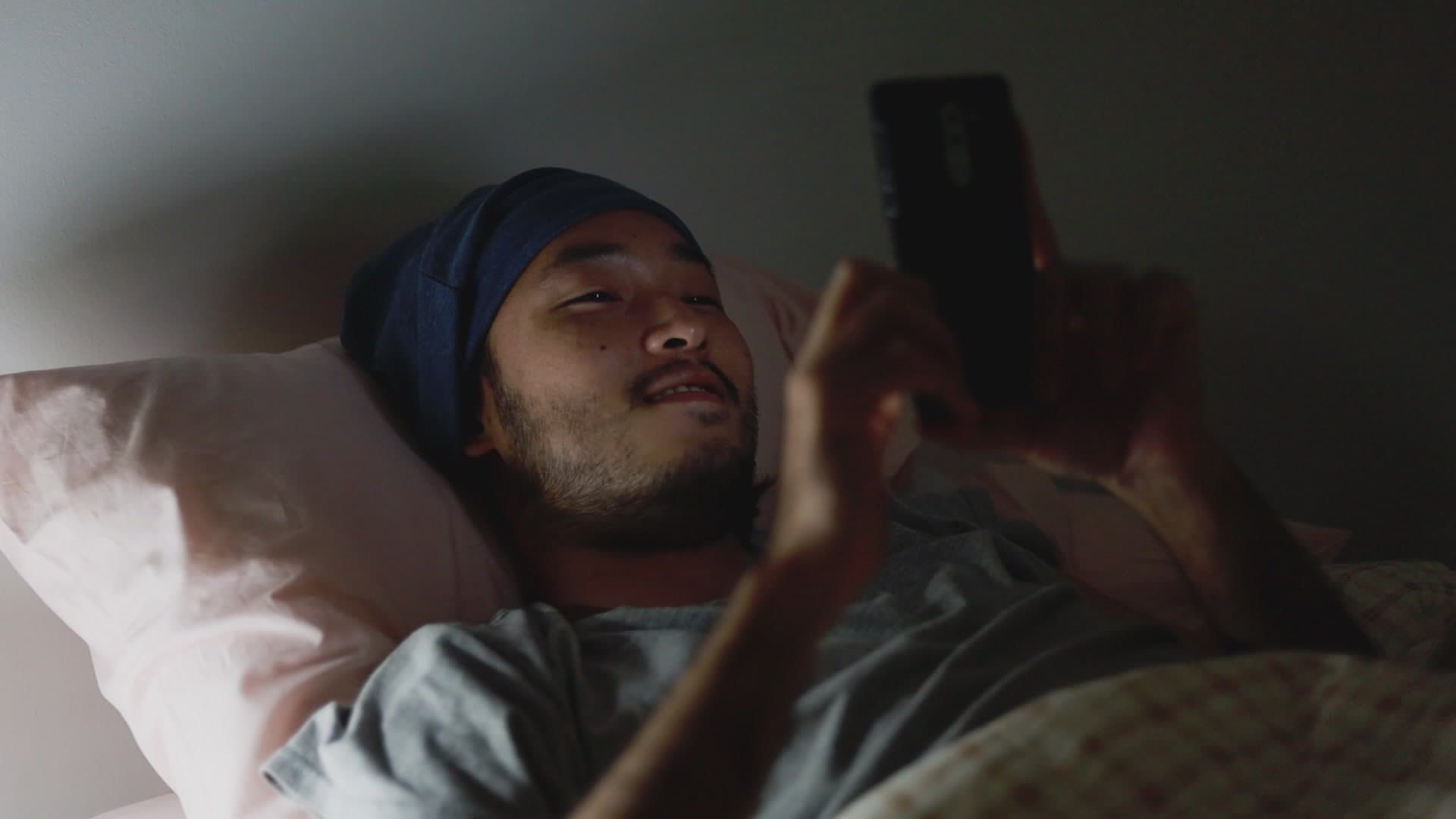 asian-man-using-a-mobile-phone-while-lying-in-bed-at-home-late-at-night-free-video-1.jpg